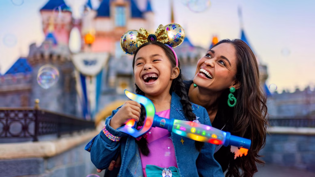 A smiling young girl and woman holding a large Key to Disneyland in front of Sleeping Beauty's Castle.
